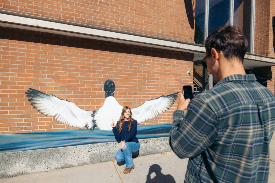 A woman taking a photo in front of a loon mural