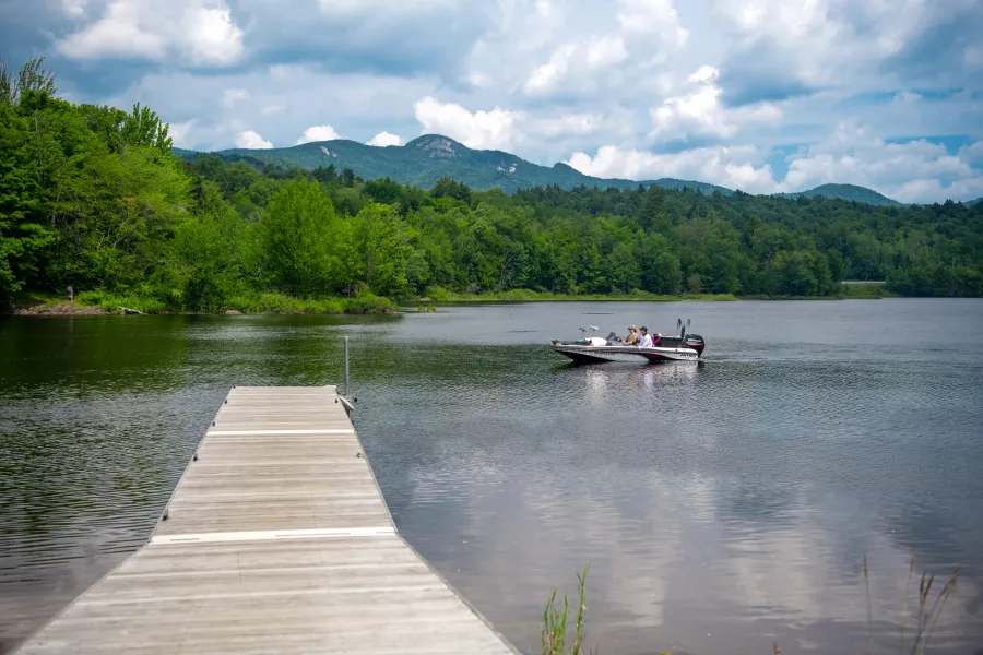 A long dock, a boat in the water, and mountains in the background