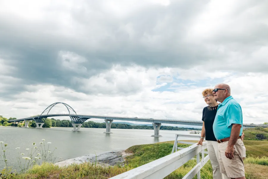 An older couple standing by a bridge over a lake