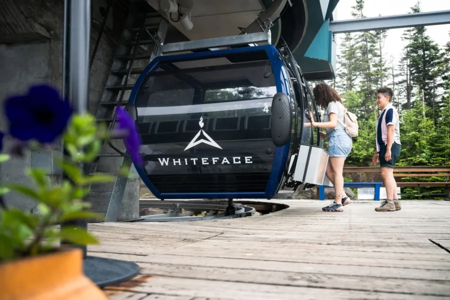 A mother and child step onto a gondola at Whiteface Mountain on a sunny summer day. 