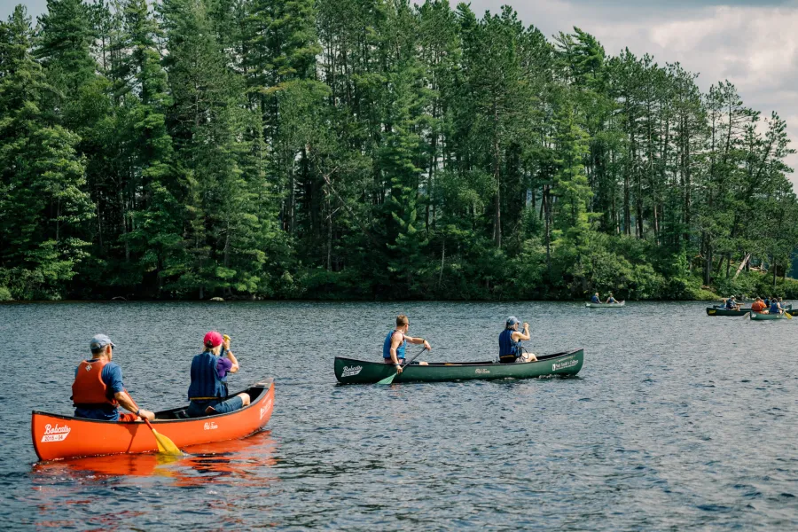 A group of people paddle in canoes on a lake. 