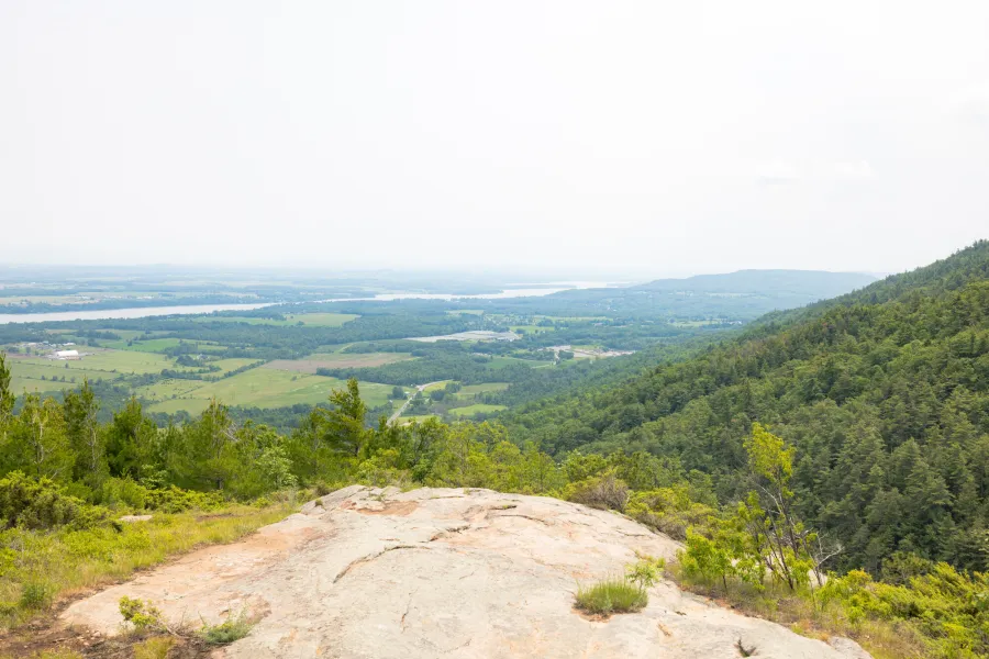 The top of a mountain looks out to green farmland and rolling hills. 