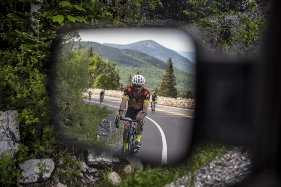 A person road cycling in a car's rearview mirror.