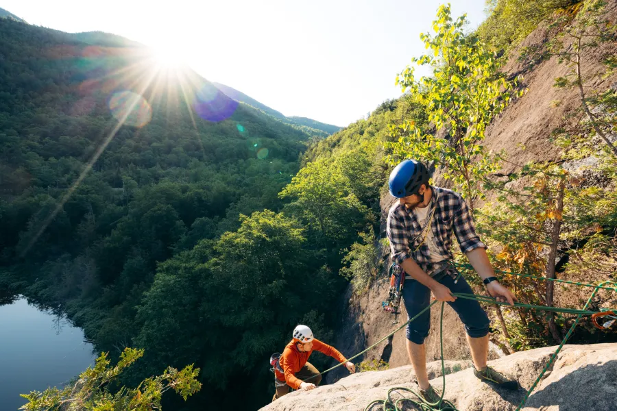 Two men mountain climb up a rock ledge. 