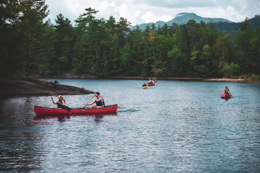 Three canoes traversing a calm Adirondack lake with trees and a mountain in the background.