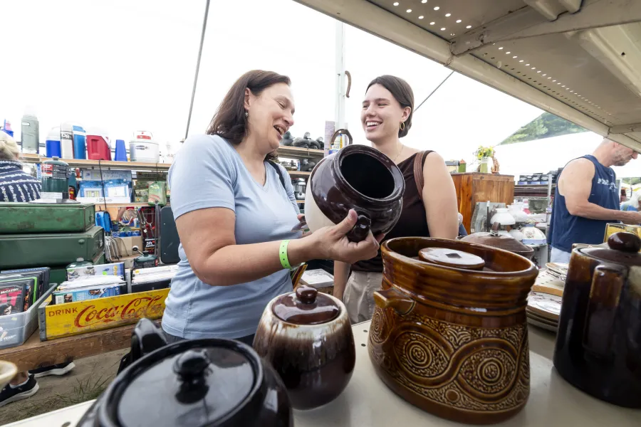 Two women smile over a table of antique crockery.