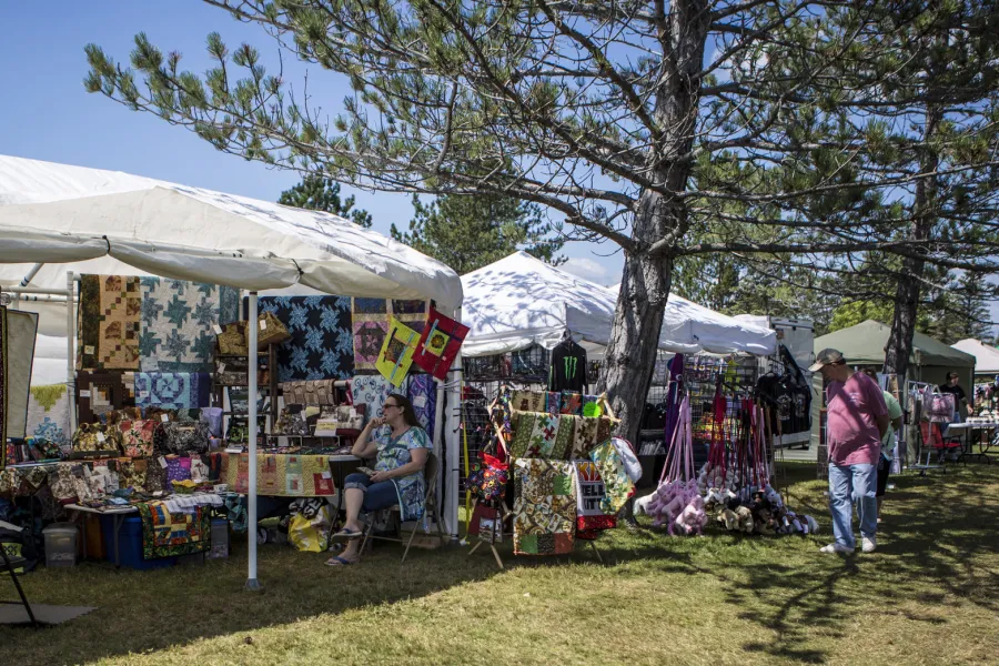 An adult walks along a row of tents selling antiques and quilts on a sunny summer day.
