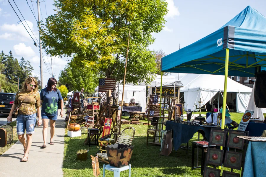 Open-air tents and antiques fill the lawn next to a sidewalk on a sunny fall day.