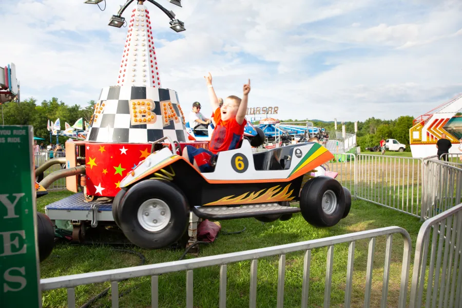 A child raises his arms in joy while riding a small, spinning carnival ride. 