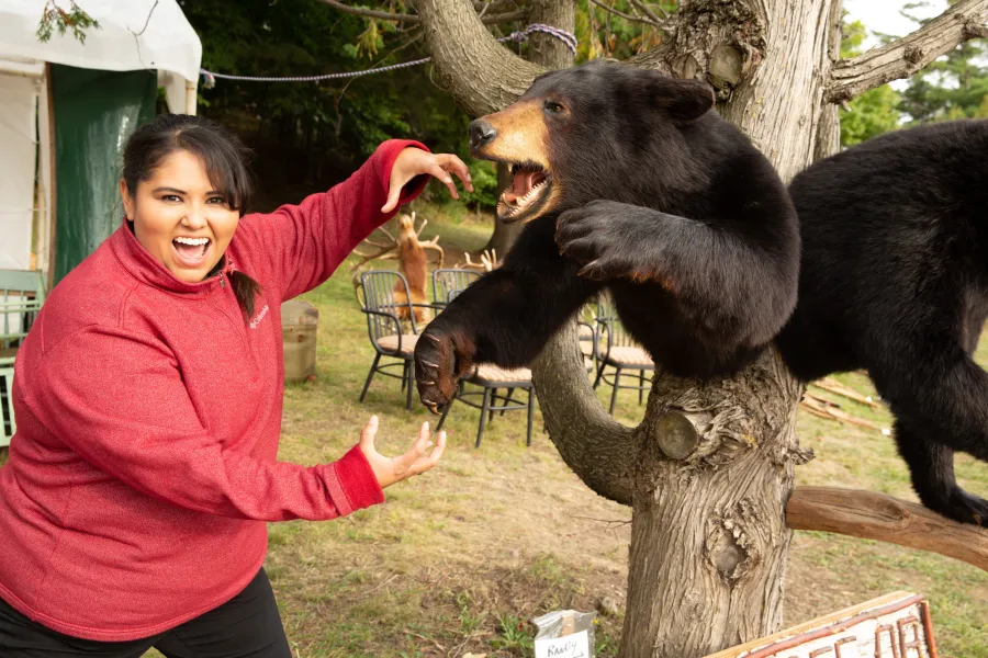 A woman poses with a taxidermied bear, making a growling face and holding her hands like claws.