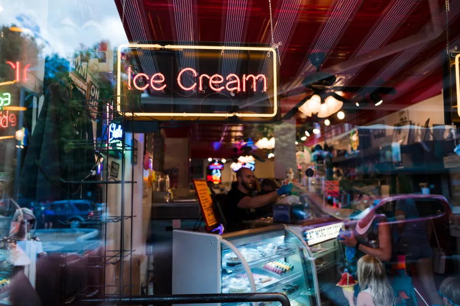 A neon ice cream sign sits in the window of an ice cream shop. 