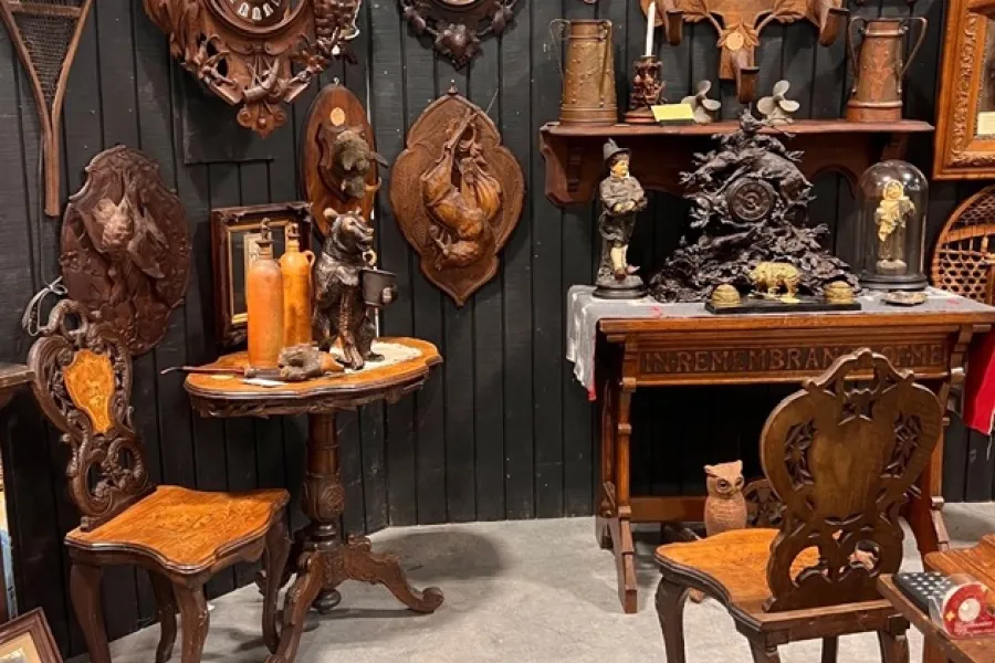 An antique show display booth shows elaborately carved, Adirondack-style antique furniture and decor.
