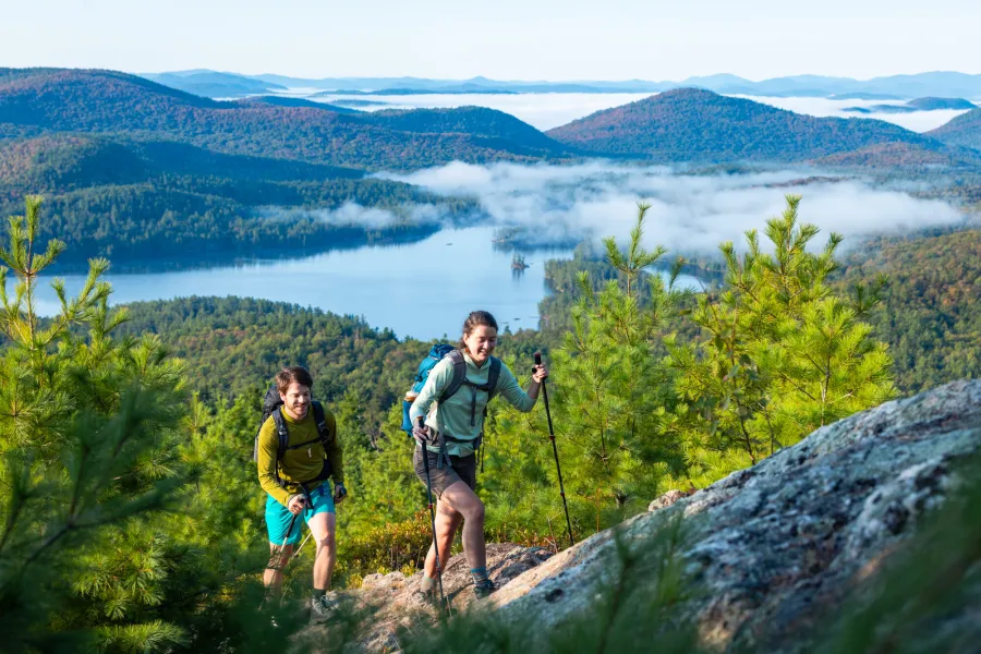 A man and woman hike up a mountain with mist in the background. 
