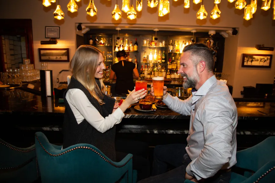 A man and woman cheers drinks at a hotel bar. 