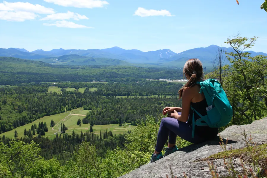 A woman sits on a rock slab overlooking a valley.