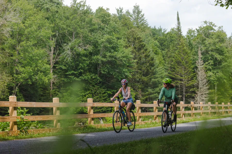 Two women ride bikes on a rail trail in summer. 
