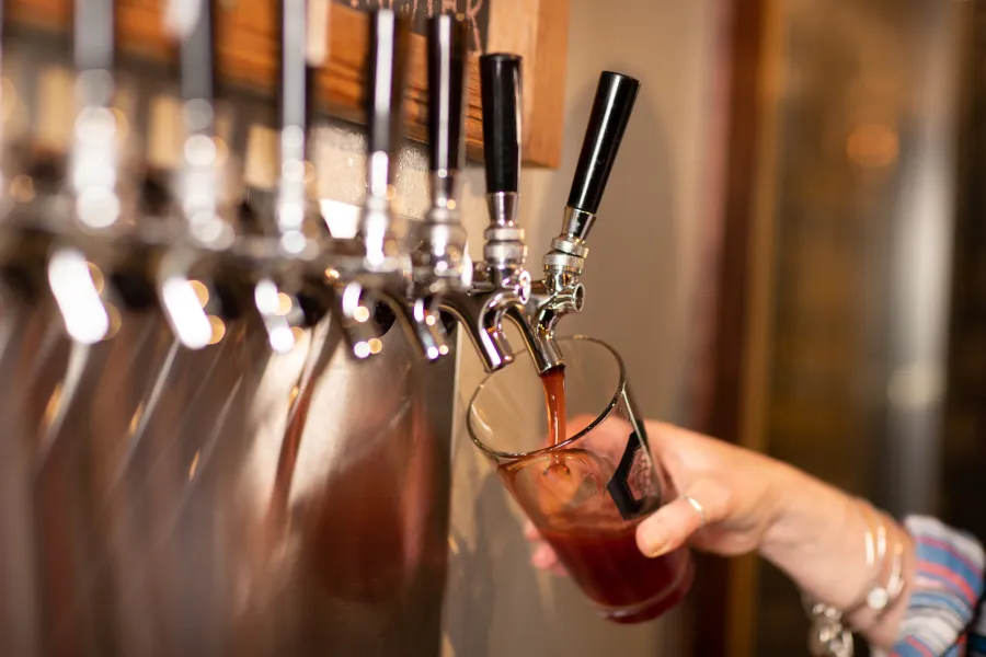A close-up of a hand filling a pint glass at a row of beer taps.